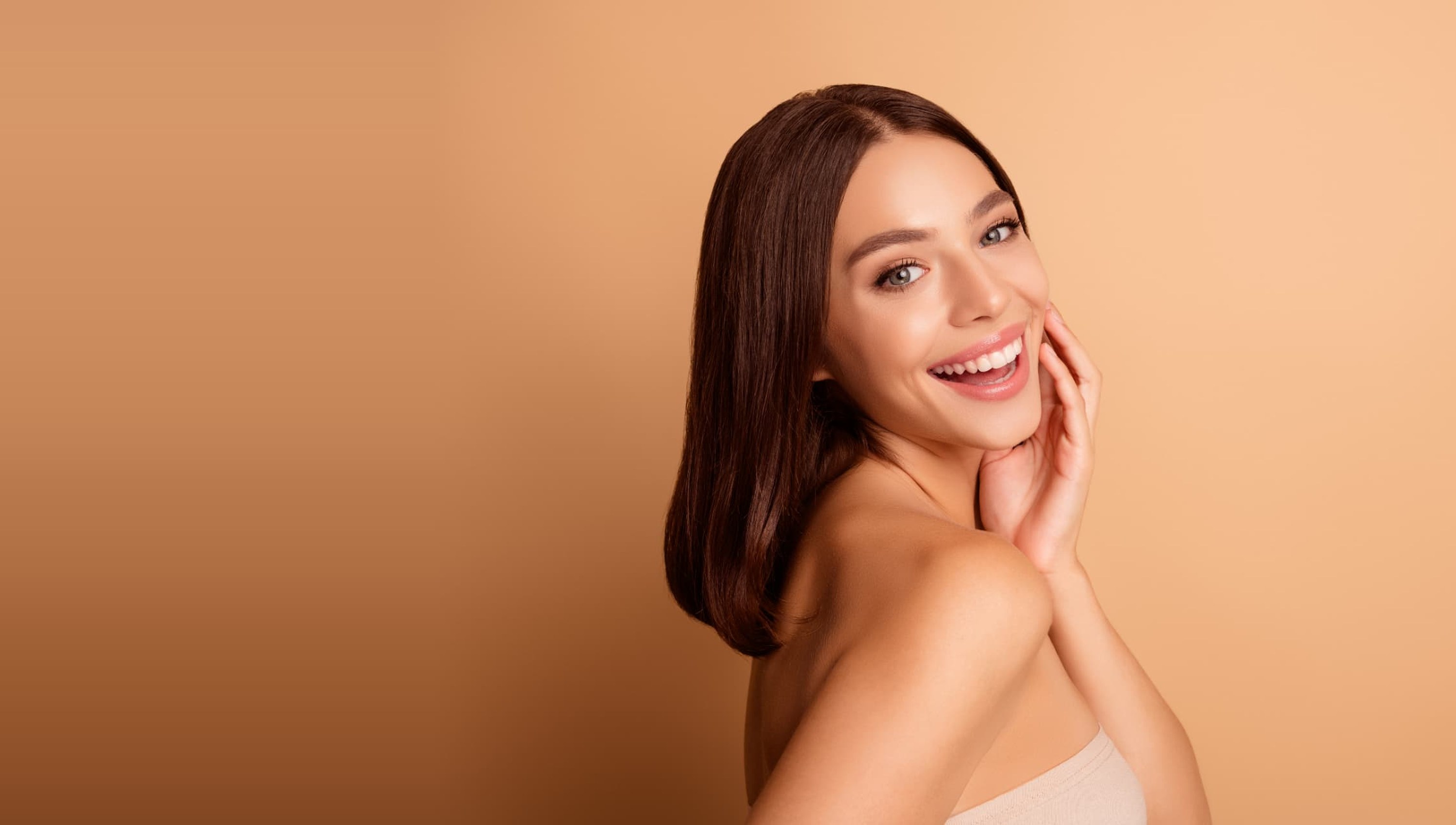 Smiling client with glowing skin against a warm beige background